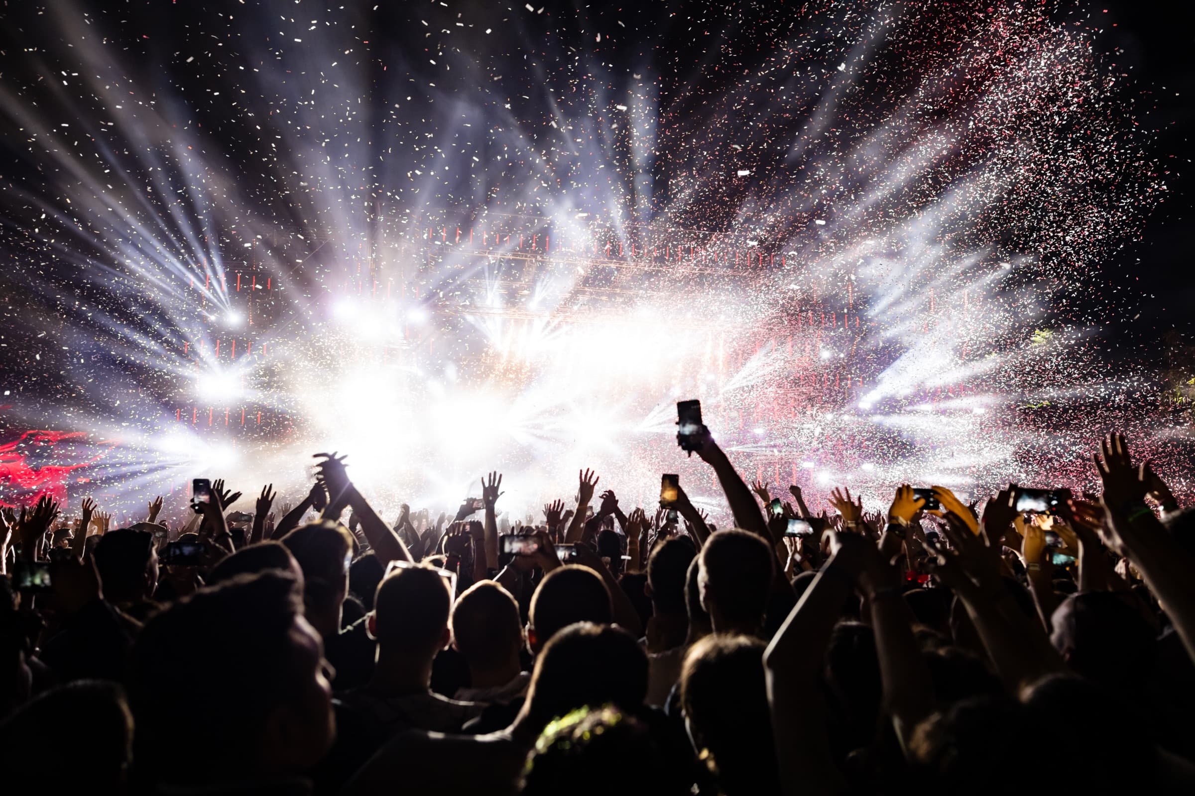 A festival crowd under confetti and stage lights at night