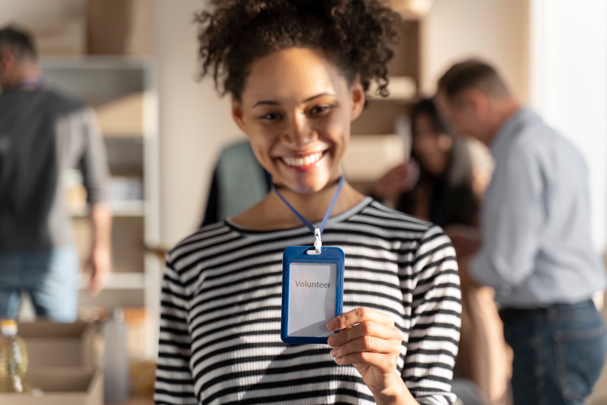A smiling volunteer holding up the ID badge on her lanyard