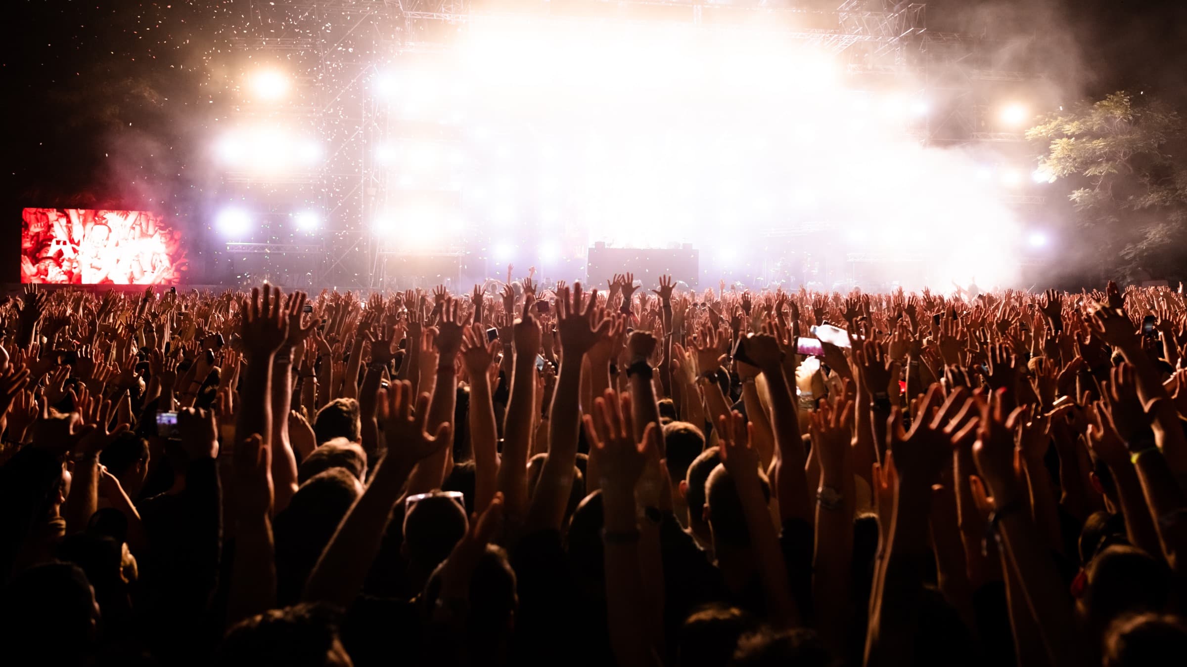 A packed festival crowd with arms raised towards a brightly lit stage